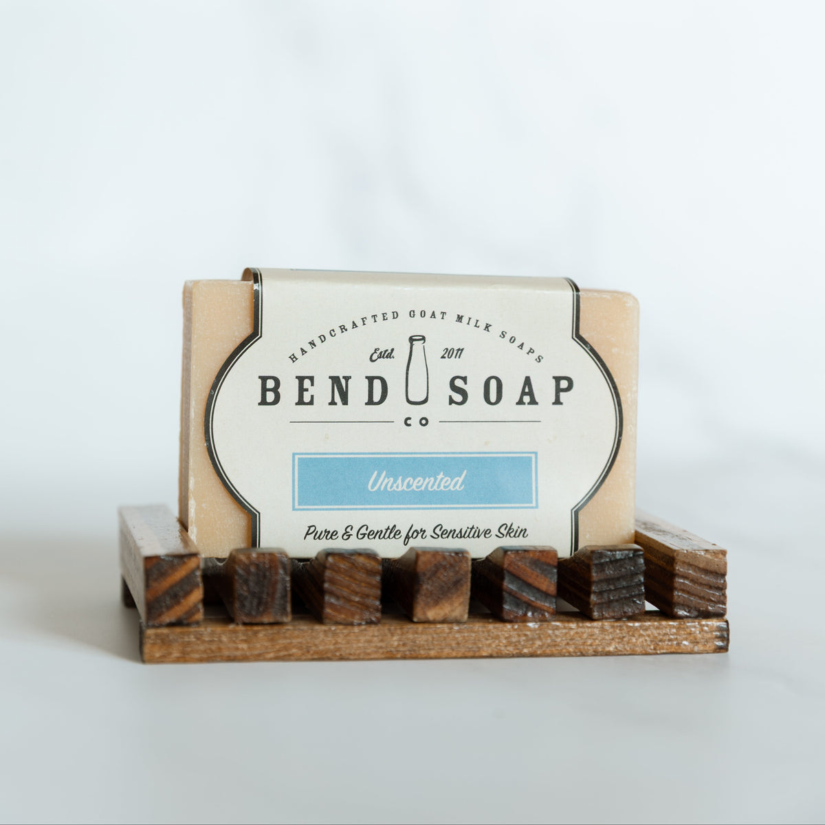 Bar of soap in a wooden holder with 'Bend Soap Co' branding on a white background