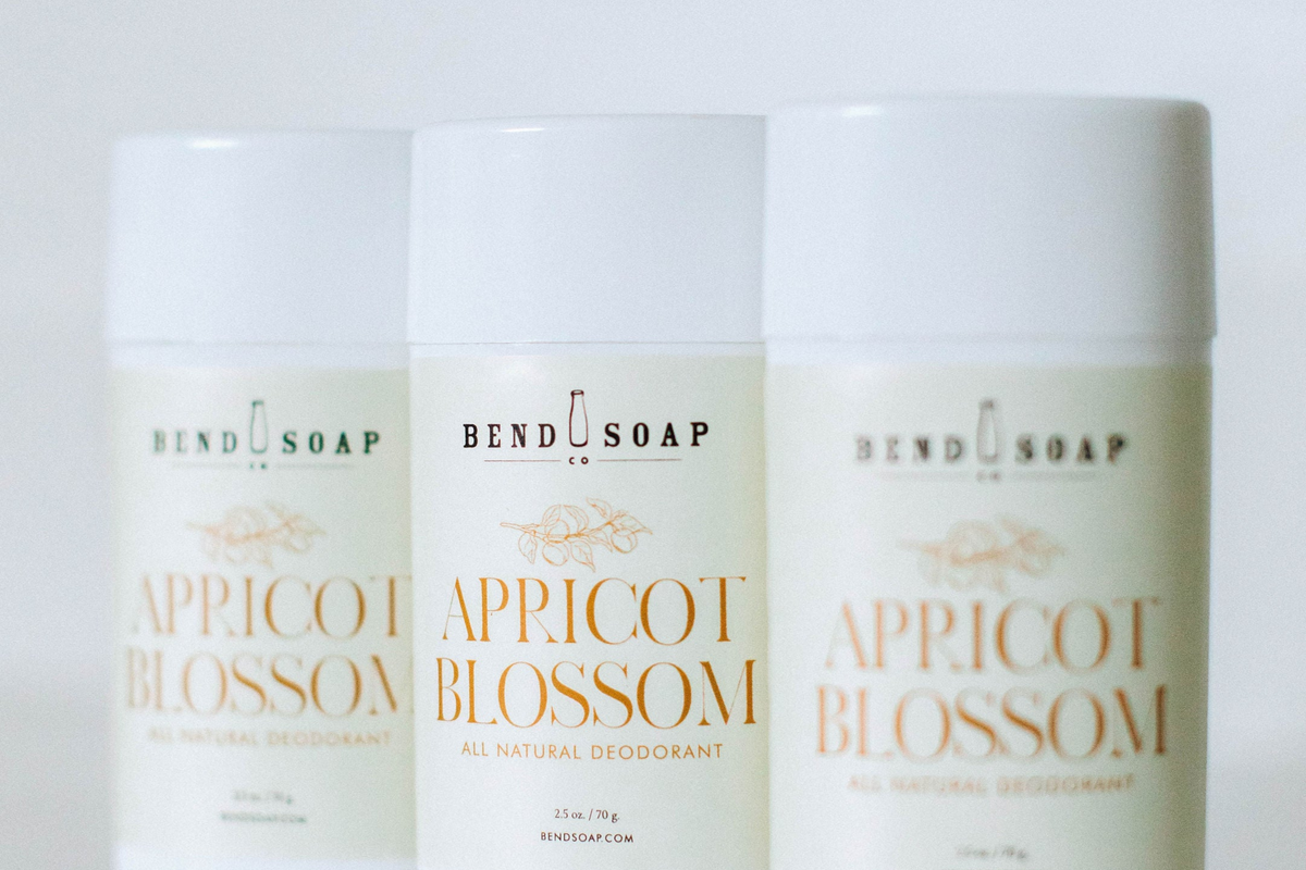 Three white tubes of Bend Soap Co. Apricot Blossom all natural deodorant are arranged side by side against a white background, with the center tube in sharp focus and the others slightly blurred.