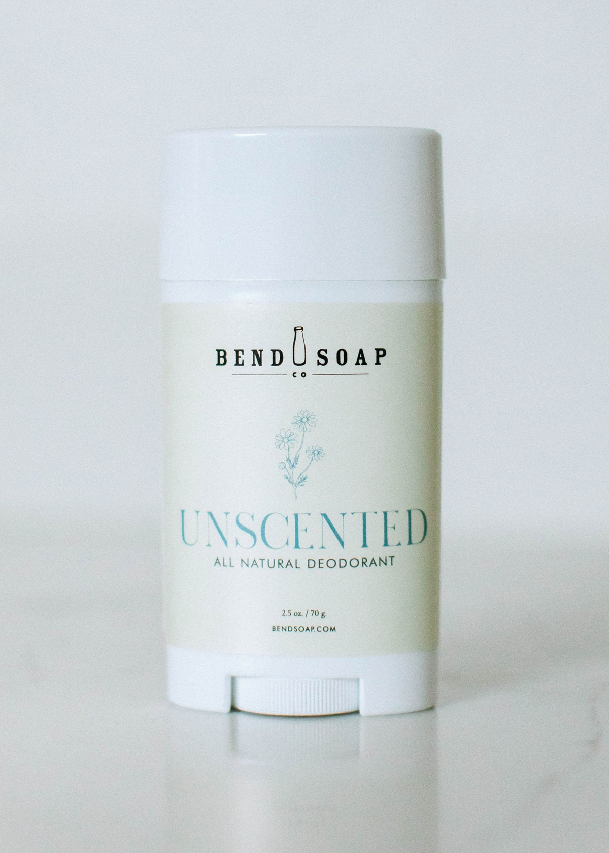 A white stick of Bend Soap unscented all natural deodorant stands upright on a light surface, featuring simple blue text and a minimalist design on its label.