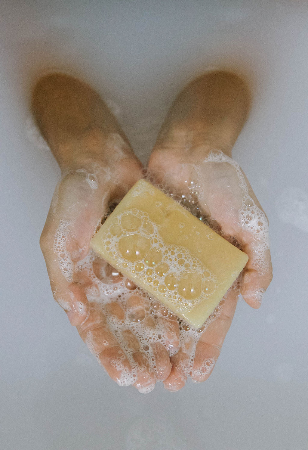 Two hands cup a bar from the Best for Men Bundle, lathered with bubbles, and submerged in milky bathwater.