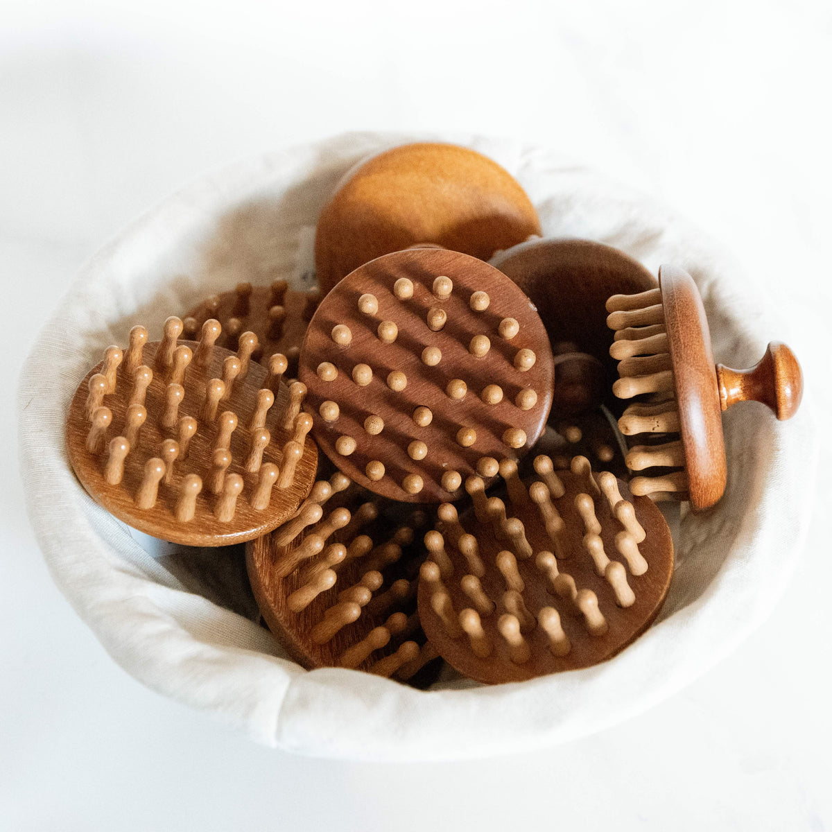 Wooden massage brushes with textured surfaces in a white bowl.