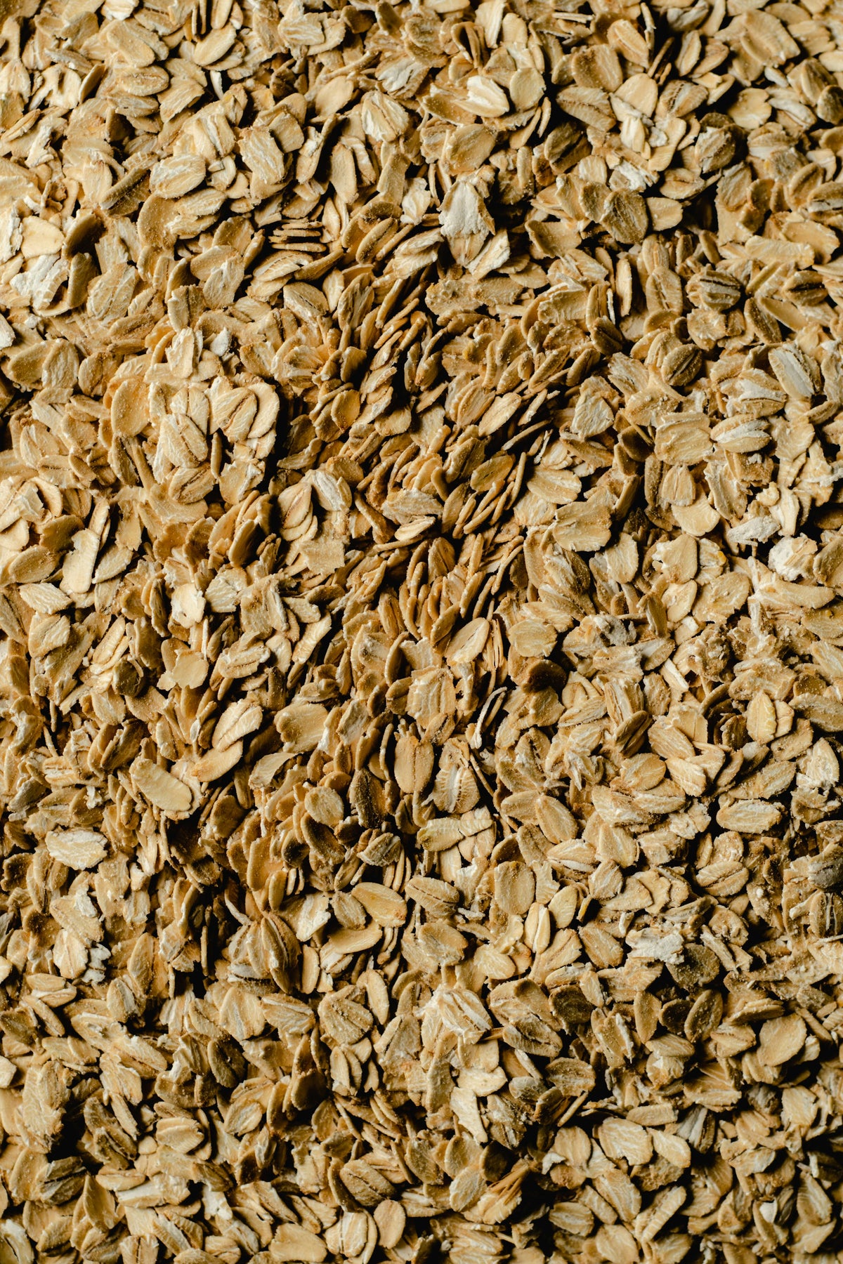 A close-up view of a large pile of dry rolled oats, showing their rough, flat texture and light brown color.