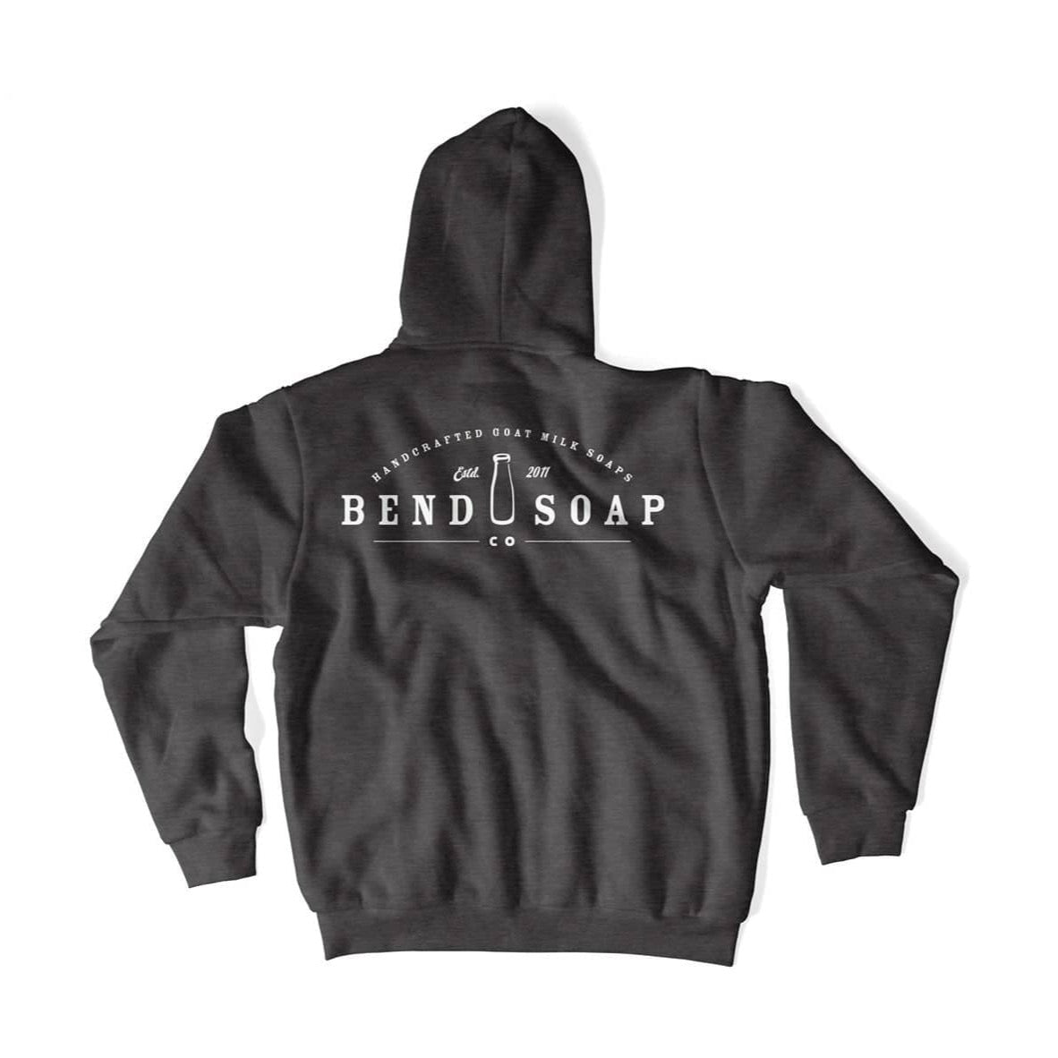 The Bend Soap Co. Unisex Zip-Up Hoodie is shown flat, back view, featuring white "Bend Soap Co." and "Handcrafted Goat Milk Soap" text with a soap bar graphic. Comes in dark gray with cozy fleece lining for extra comfort.